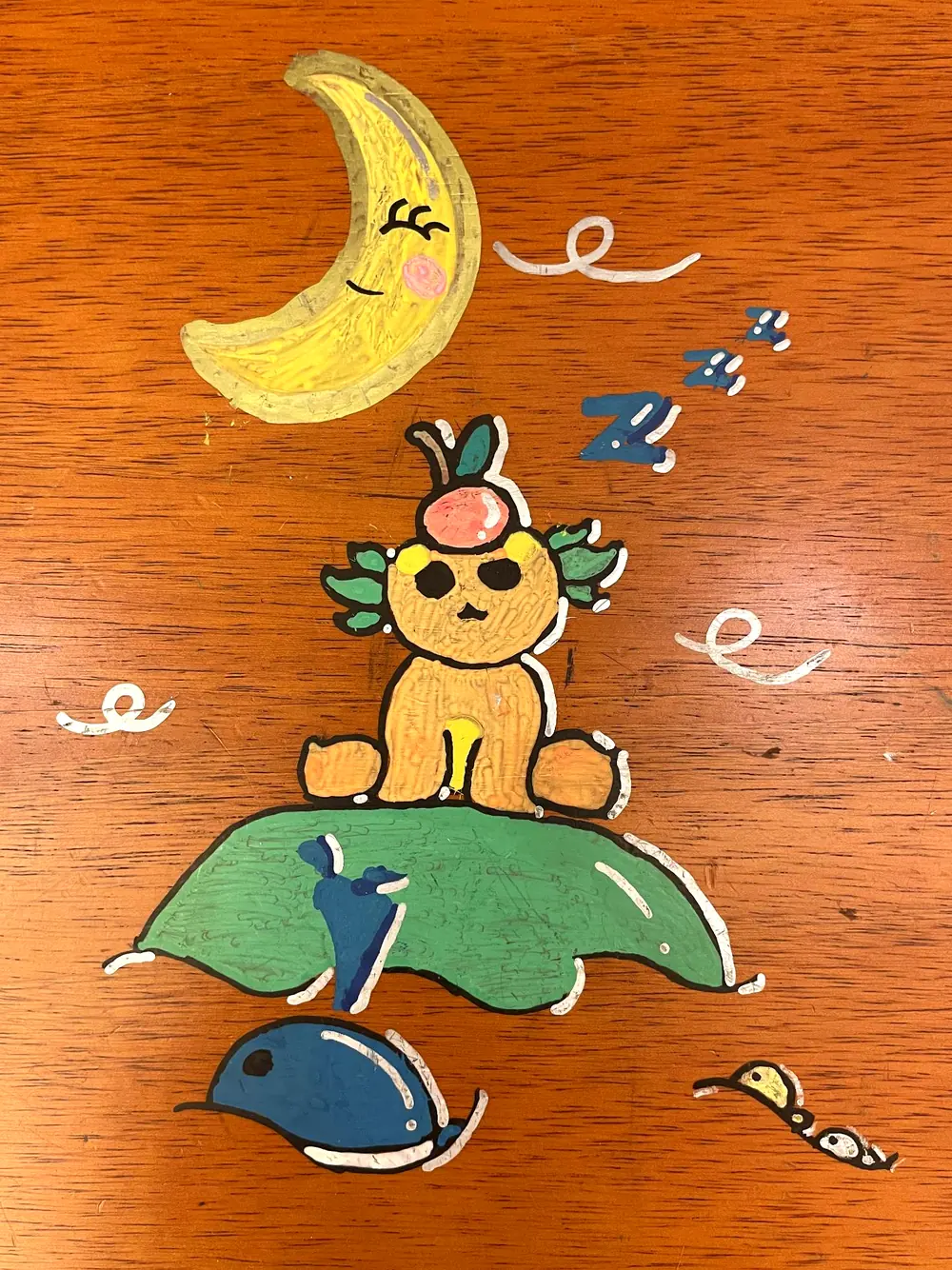 侄女 9 岁时画在木桌上的海猫精灵：坐在一片大叶子上，头顶苹果，旁边是月亮、鲸鱼和几条鱼